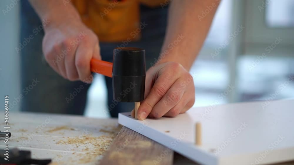 Man clogging wooden dowel into furniture board using mallet Man clogging wooden dowel into furniture board using mallet