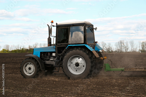 Tractor with planter cultivating field on sunny day. Agricultural industry