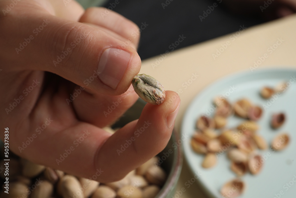 Woman holding tasty peeled pistachio nut over bowl, closeup. Space for text Woman holding tasty peeled pistachio nut over bowl, closeup. Space for text