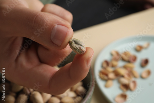 Woman holding tasty peeled pistachio nut over bowl, closeup. Space for text
