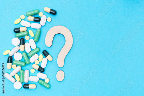 Wooden question mark and different drugs with pills on a blue background. Treatment choice concept. Flat lay. Top view. Place for text. Copy space.