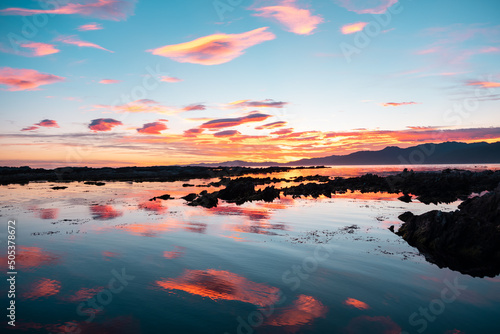 Beautiful clouds in blue sky with reflection in the water and orange sunset on the sea, Kaikoura, South Island, New Zealand