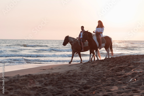a loving couple in summer clothes riding a horse on a sandy beach at sunset. Sea and sunset in the background. Selective focus 
