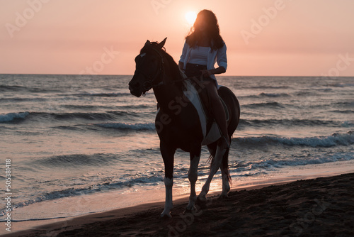 Woman in summer clothes enjoys riding a horse on a beautiful sandy beach at sunset. Selective focus  © .shock
