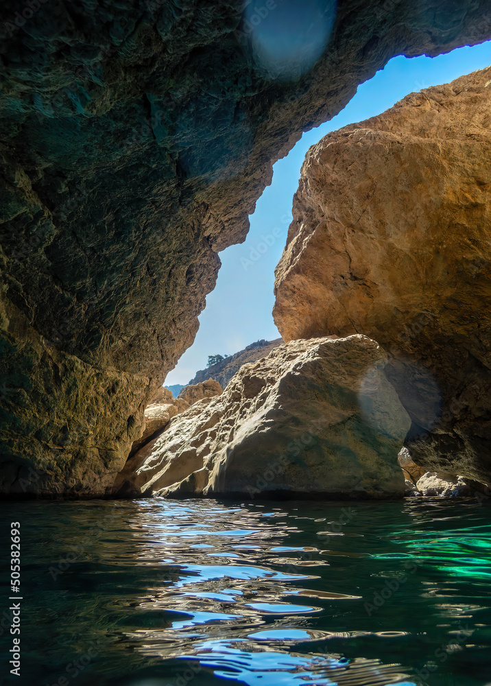 Lens flare and sea water shining under the rays of the sun inside a sea cave. Summer on a Greek island. Lens flare and sea water shining under the rays of the sun inside a sea cave. Summer on a Greek island.