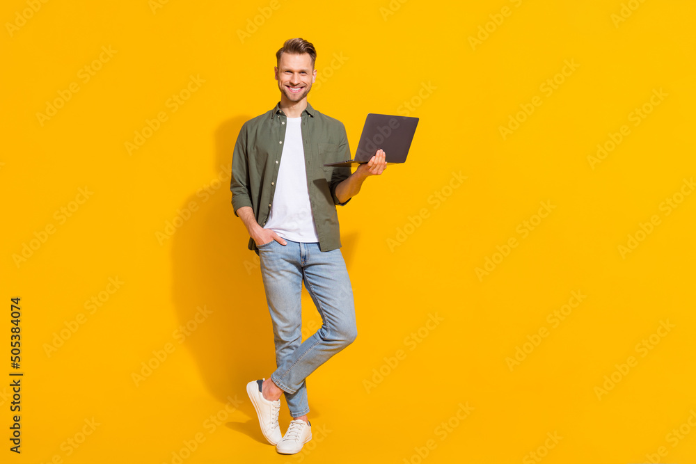 Full length body size view of attractive cheerful guy using laptop booking order isolated over bright yellow color background - obrazy, fototapety, plakaty 