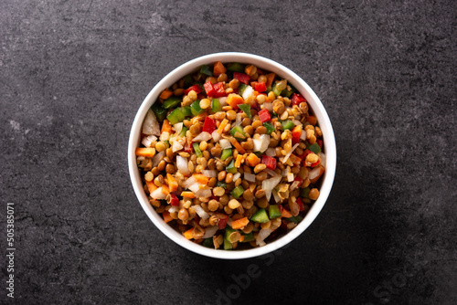 Lentil salad with peppers,onion and carrot in bowl on black background. Top view
