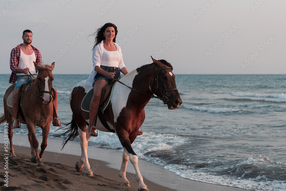 a loving couple in summer clothes riding a horse on a sandy beach at sunset. Sea and sunset in the background. Selective focus a loving couple in summer clothes riding a horse on a sandy beach at sunset. Sea and sunset in the background. Selective focus