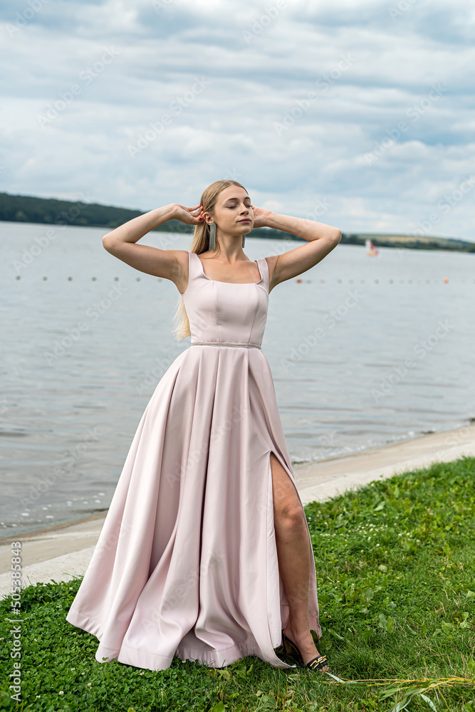 Young woman in long pink evening dress standing alone near lake at city park Young woman in long pink evening dress standing alone near lake at city park