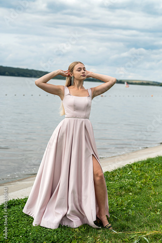Young woman in long pink evening dress standing alone near lake at city park © RomanR