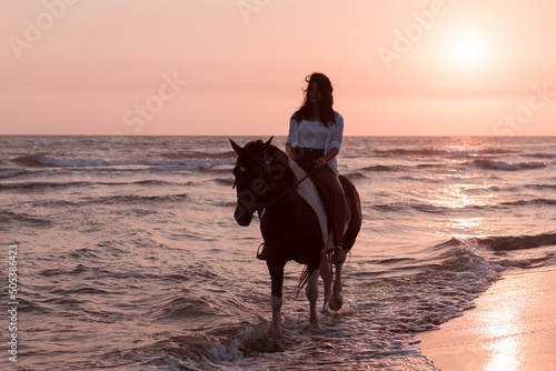 Woman in summer clothes enjoys riding a horse on a beautiful sandy beach at sunset. Selective focus 