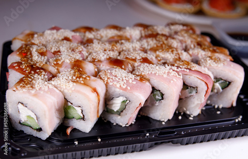 A portion of sushi with fish, rice and sesame seeds on a plastic backing.