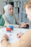 Selective focus shot of Muslim woman wearing hijab working as consular officer in embassy having appointment with unrecognizable man