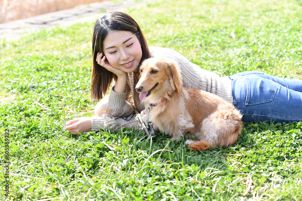 Φωτογραφία 芝生の上で愛犬と寝転ぶ若い女性
