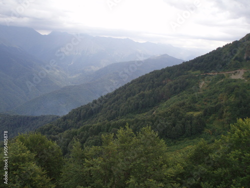A panorama mountain landscape with valleys and forest mountain peaks under an overcast and cloudy sky