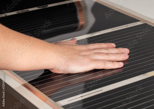 A man checks with his hand the heat from the infrared floor heating after installation. Close-up photo