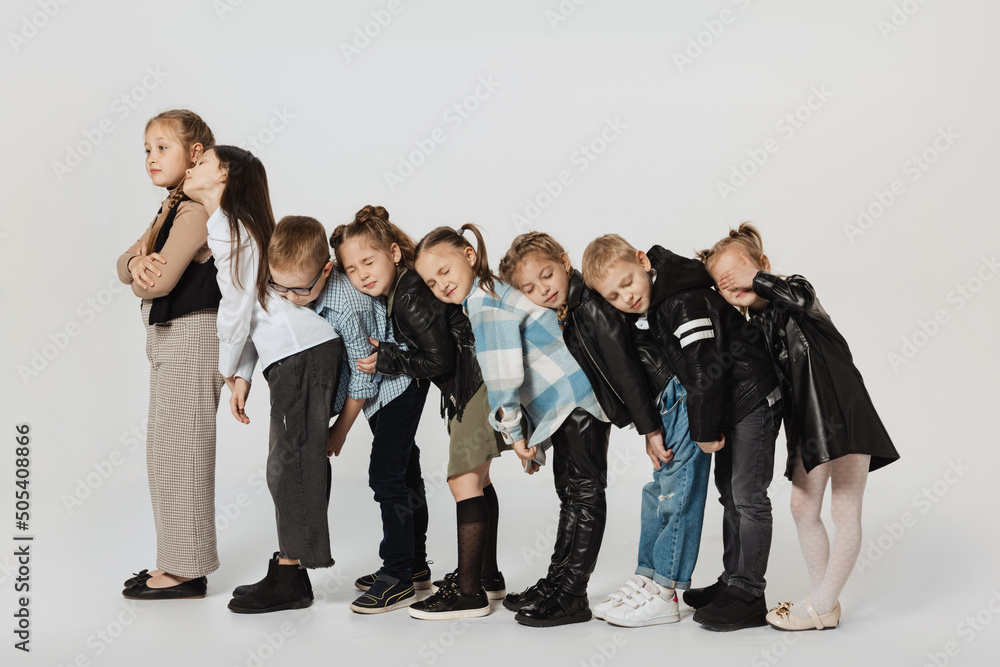 Obraz premium Group of happy cute kids, little girls and boys in modern outfits standing isolated on grey studio background. Beauty, kids fashion, education, happy childhood concept.
