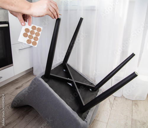 A man glues protective pads on the legs of a chair. Protection against floor scratches and noise photo