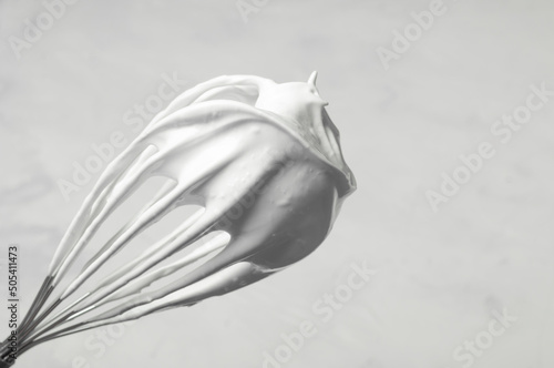 corolla with whipped cream or whipped egg whites on a gray background, the whisk is located diagonally, copy space. photo