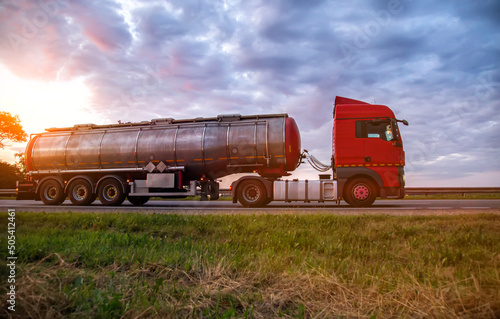 A modern truck with a semi-trailer tanker transports dangerous goods against the backdrop of a sunset in summer. Liquid cargo transportation. Copy space for text, sanctions
