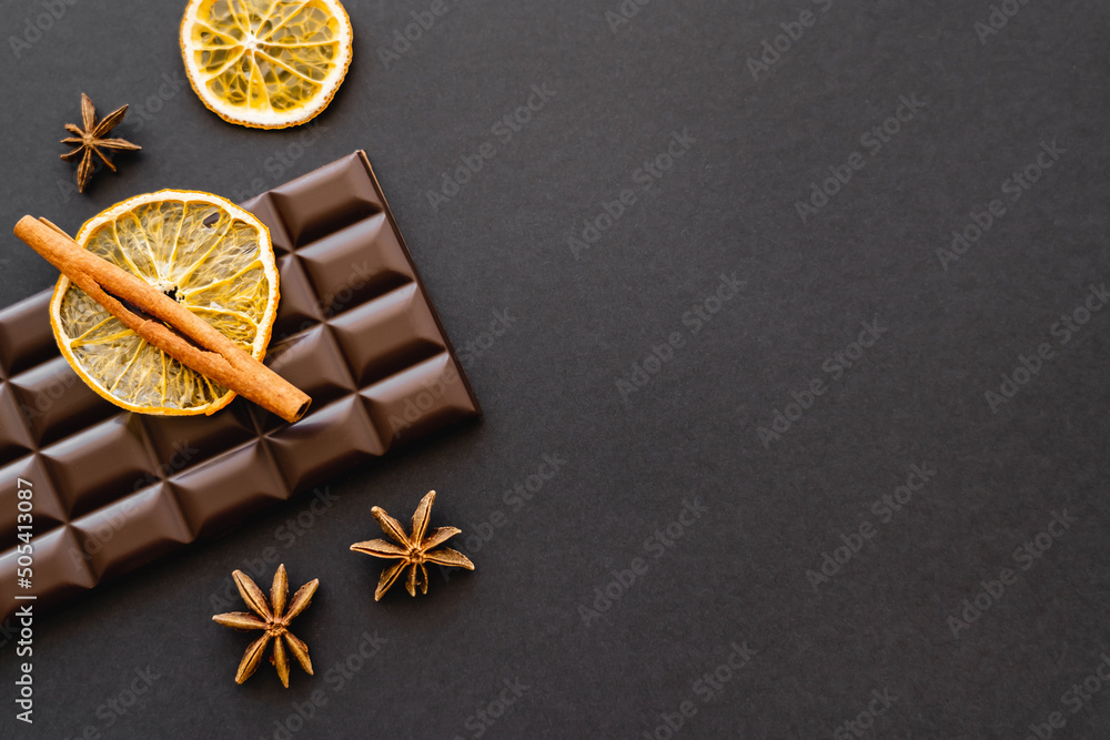 Fototapeta premium Top view of cinnamon, anise and orange slice on chocolate on black background.