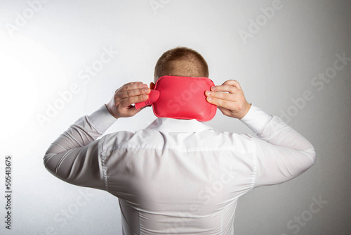 A man holds a heating pad with hot water on the back of his head. Muscle relaxation and vasodilatation of the head, thermotherapy. Headache treatment, close-up photo