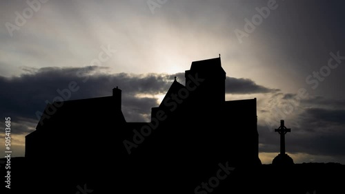 Iona abbey in Scotland, Time Lapse at Sunrise with Fast Clouds and Dark Silhouette of Medieval Church photo