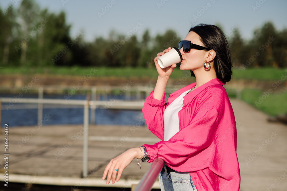 Happy brunette woman in sunglasses walking near the lake on wooden pier in sunny day