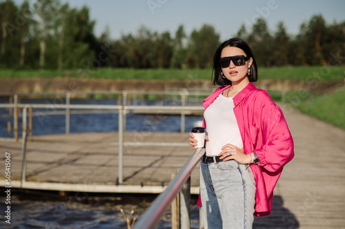 Happy brunette woman in sunglasses walking near the lake on wooden pier in sunny day