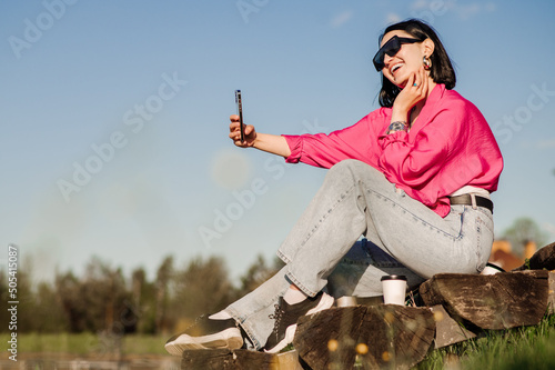 Happy brunette woman in sunglasses take selfie using cellphone over the blue sky outdoor in the park