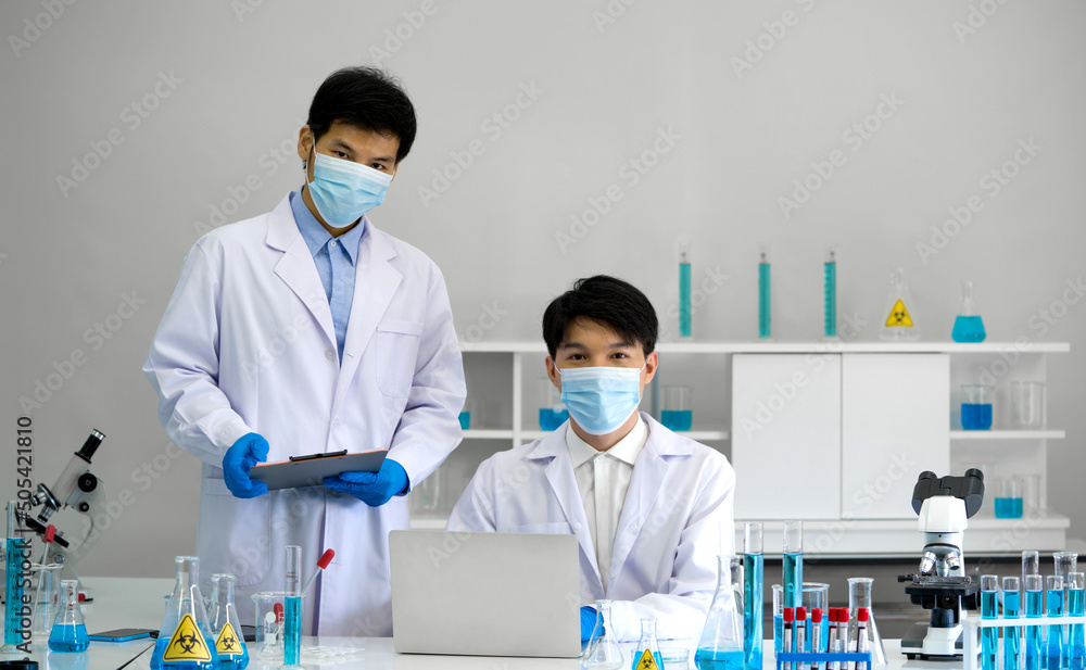 Two scientists with face mask and gown working in laboratory. Omicron strain testing process, Coronavirus disease 2019. Two scientists with face mask and gown working in laboratory. Omicron strain testing process, Coronavirus disease 2019.