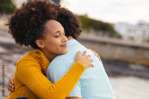 Afro young woman with eyes closed hugging african american boyfriend at beach photo