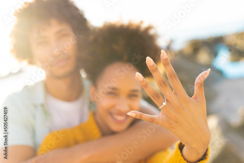 Cheerful excited woman showing off her engagement ring with african american boyfriend at beach photo