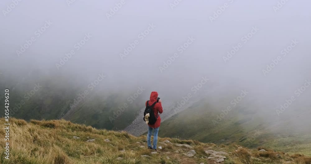 young girl with a backpack, stands in the mountains on the edge of a cliff and do something on a smartphone, online shopping, correspondence. Strong cloud cover, wind, bad weather. Carpathians young girl with a backpack, stands in the mountains on the edge of a cliff and do something on a smartphone, online shopping, correspondence. Strong cloud cover, wind, bad weather. Carpathians