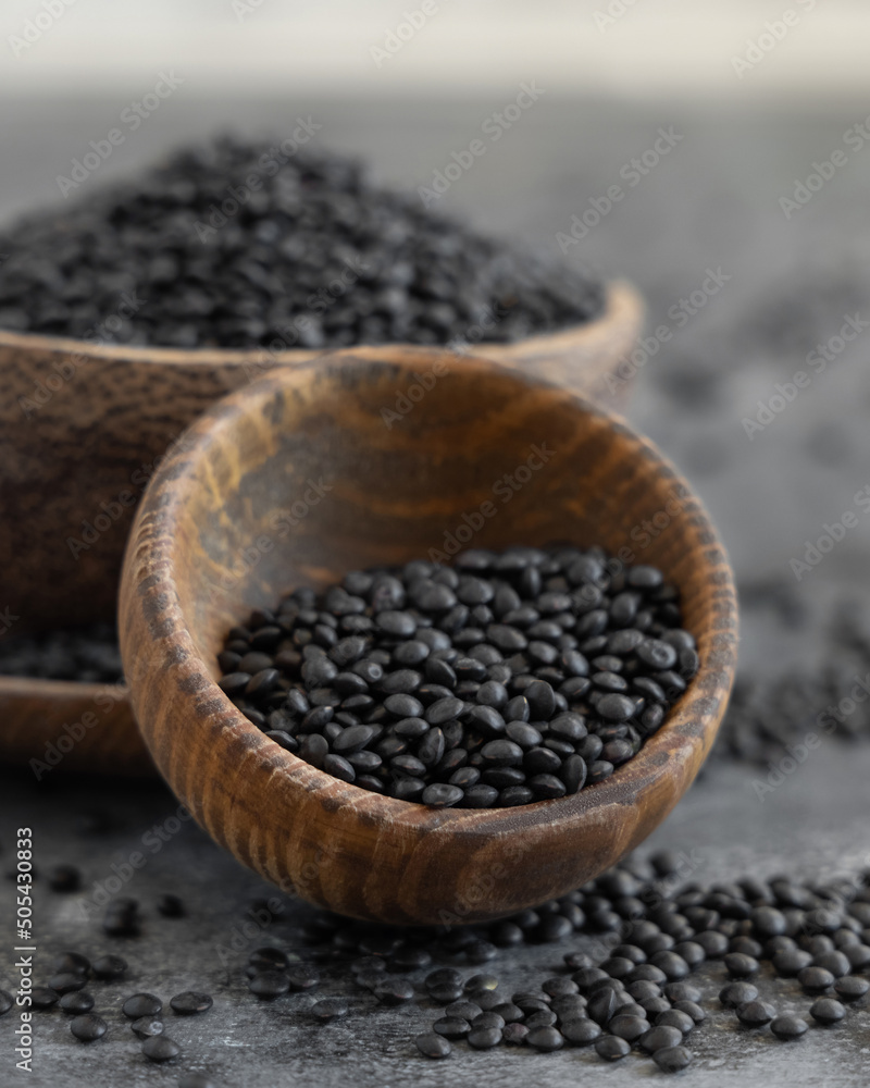 Wooden bowls of dry black lentils beans on grey table close up, protein source for vegetarian diet Wooden bowls of dry black lentils beans on grey table close up, protein source for vegetarian diet