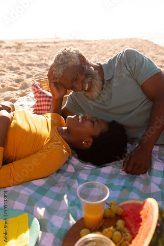 Romantic happy african american couple looking at each other while lying on blanket at beach