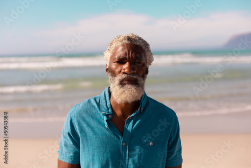 Portrait of serious bearded african american senior man with gray hair standing against sea and sky