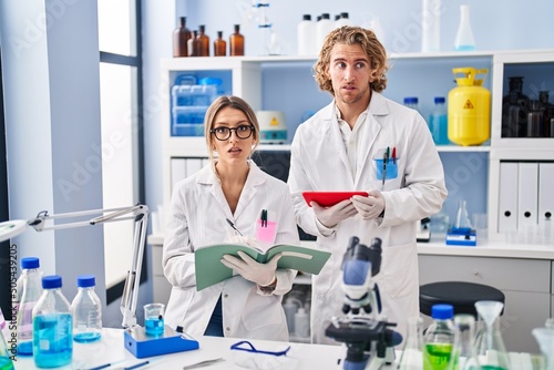 Two people working at scientist laboratory clueless and confused expression. doubt concept.