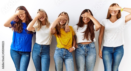Group of young girl friends standing together over isolated background smiling and laughing with hand on face covering eyes for surprise. blind concept.
