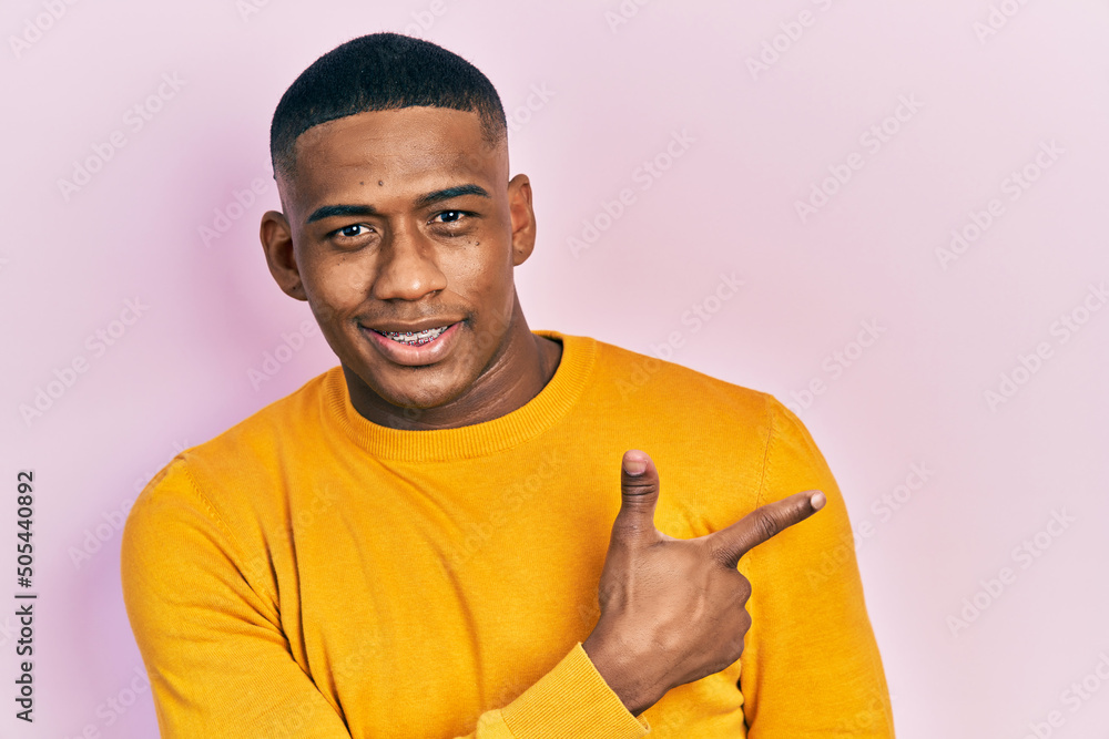 Young black man wearing casual yellow sweater smiling cheerful pointing with hand and finger up to the side Young black man wearing casual yellow sweater smiling cheerful pointing with hand and finger up to the side