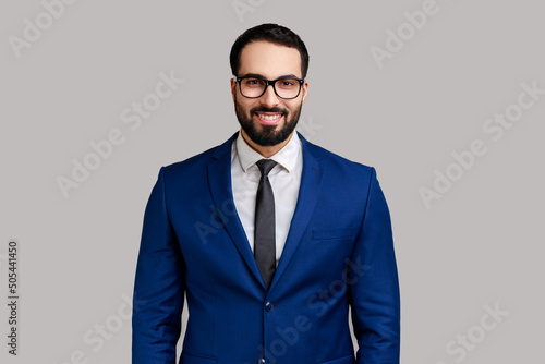 Portrait of happy smiling satisfied bearded businessman in eyeglasses, looking at camera with positive expression, wearing official style suit. Indoor studio shot isolated on gray background. photo