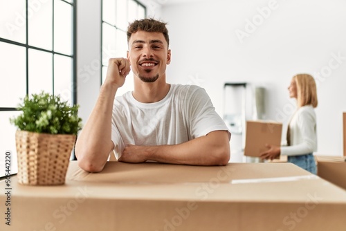 Young man smiling happy leaning on carboard box at new home.