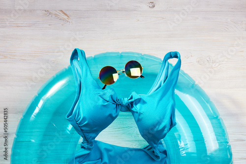 Accessories for swimming and summer holidays on a wooden background: an inflatable circle, a swimsuit and sunglasses. Top view.