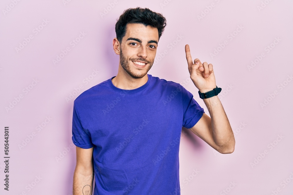 Young hispanic man wearing casual t shirt pointing finger up with successful idea. exited and happy. number one. Young hispanic man wearing casual t shirt pointing finger up with successful idea. exited and happy. number one.