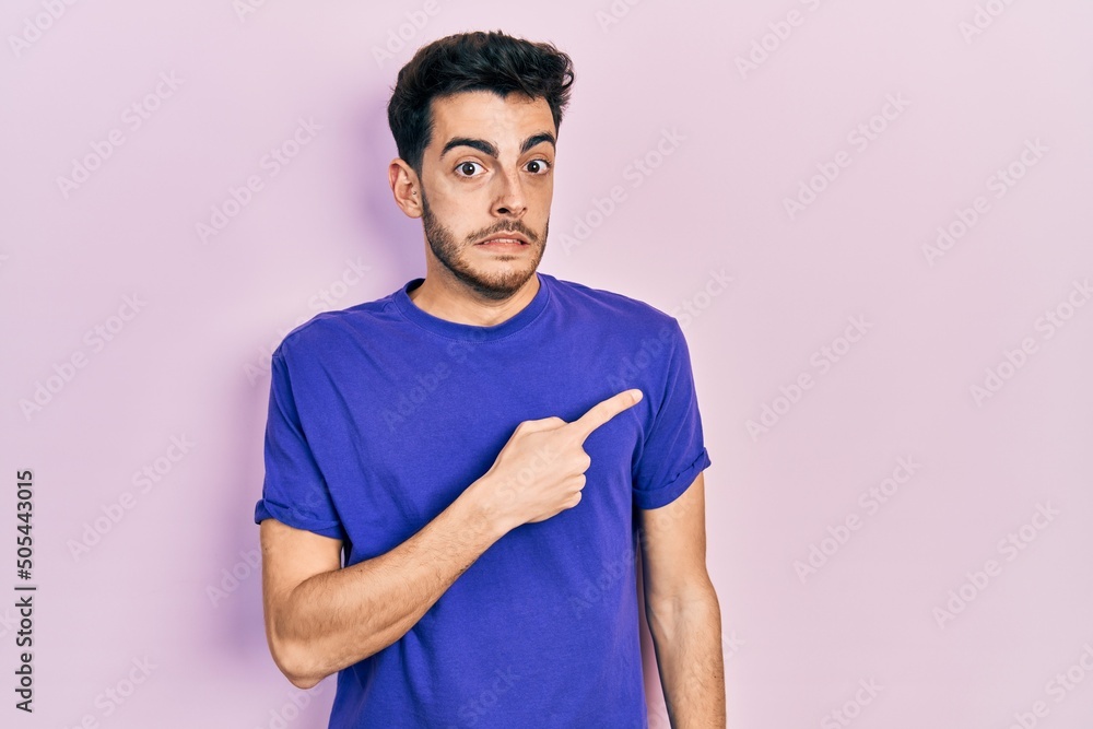 Young hispanic man wearing casual t shirt pointing aside worried and nervous with forefinger, concerned and surprised expression