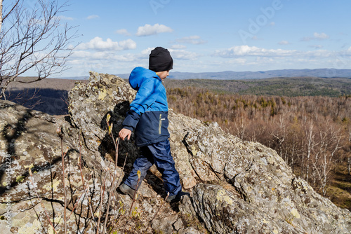 The boy confidently walks through the mountains in a hiking trip, outdoor activities, summer holidays, warm clothes, blue color, high in the mountains, children's sports mountaineering