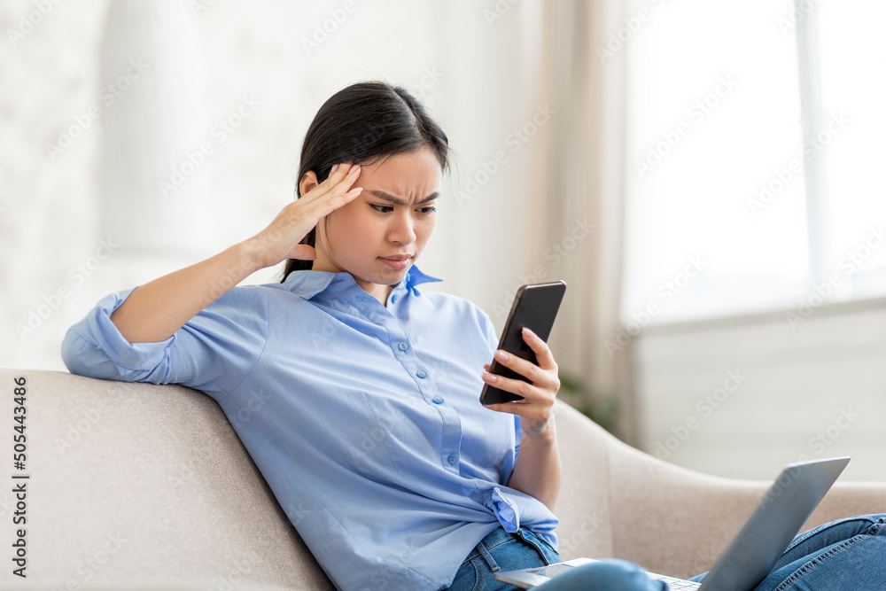 Puzzled asian business woman using laptop and smartphone at home Puzzled asian business woman using laptop and smartphone at home