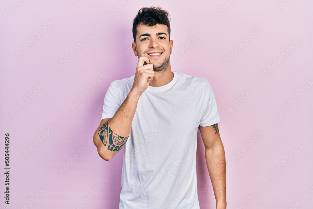 Young hispanic man wearing casual white t shirt smiling looking confident at the camera with crossed arms and hand on chin. thinking positive. Young hispanic man wearing casual white t shirt smiling looking confident at the camera with crossed arms and hand on chin. thinking positive.