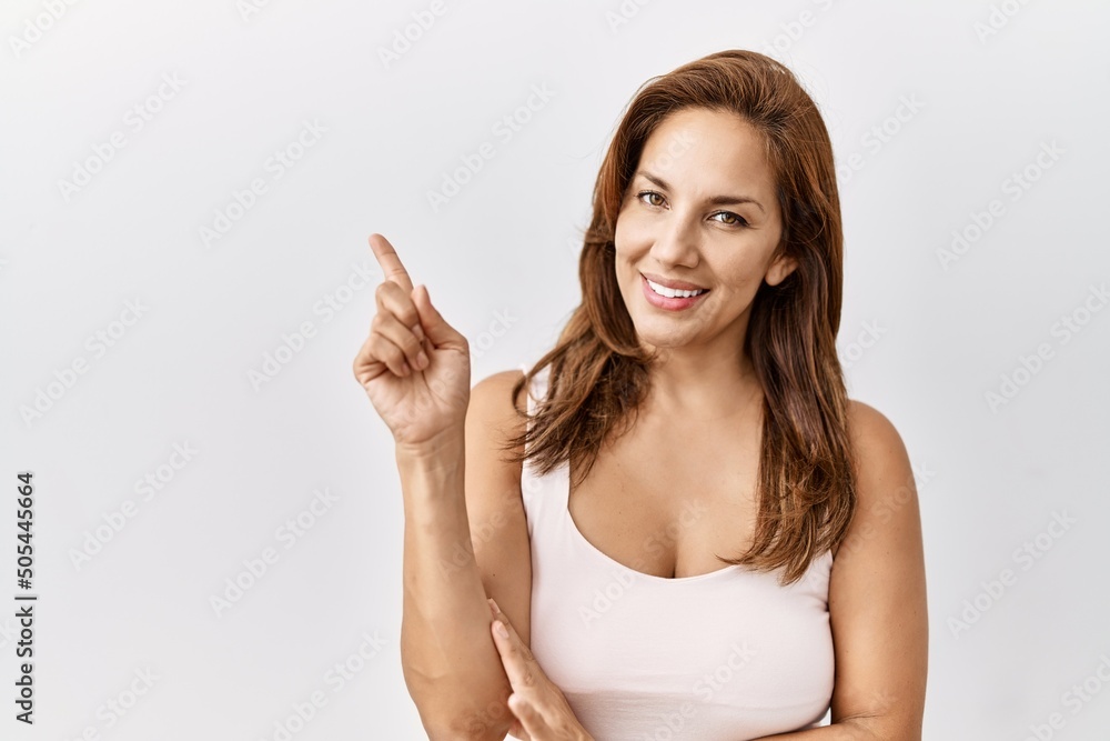 Middle age hispanic woman standing over isolated background with a big smile on face, pointing with hand and finger to the side looking at the camera. Middle age hispanic woman standing over isolated background with a big smile on face, pointing with hand and finger to the side looking at the camera.