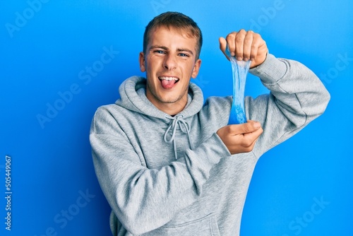 Young caucasian man holding slime sticking tongue out happy with funny expression.